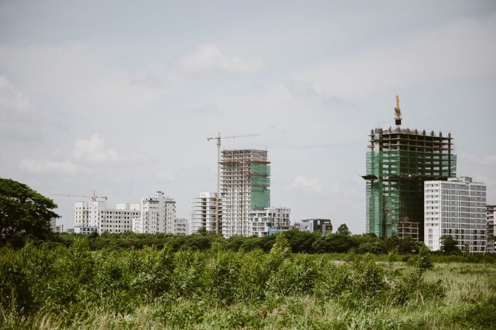 High-rise buildings under construction with cranes in a green landscape.